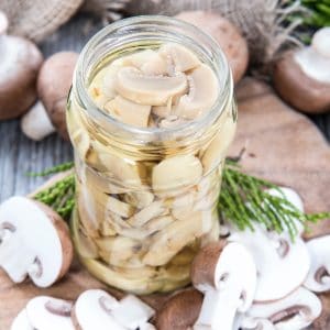 preserved mushrooms in a jar with fresh mushrooms around