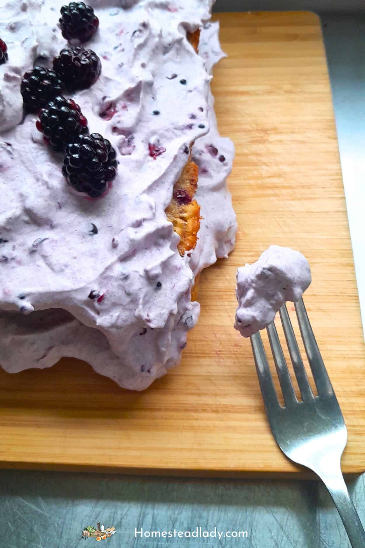 putting blackberry whipped cream on sourdough blackberry cake